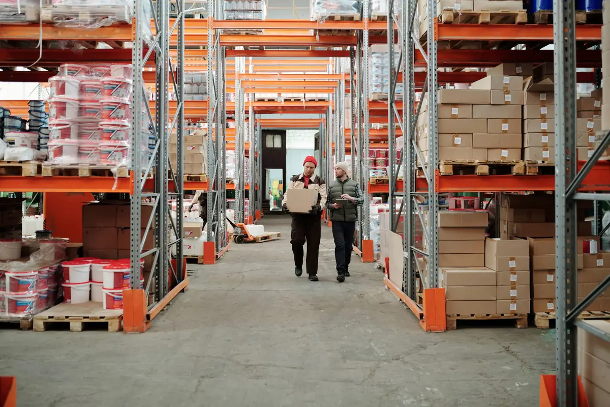 Deux opérateurs portent un carton dans une allée de stockage